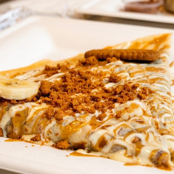 Sweet crepe drizzled with white chocolate and caramel, topped with banana slices and cookie crumbles.